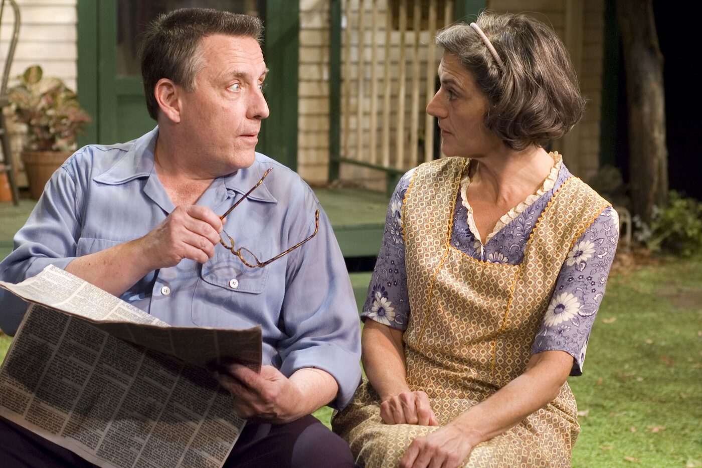 A man reading a newspaper beside a woman on the porch in All My Sons