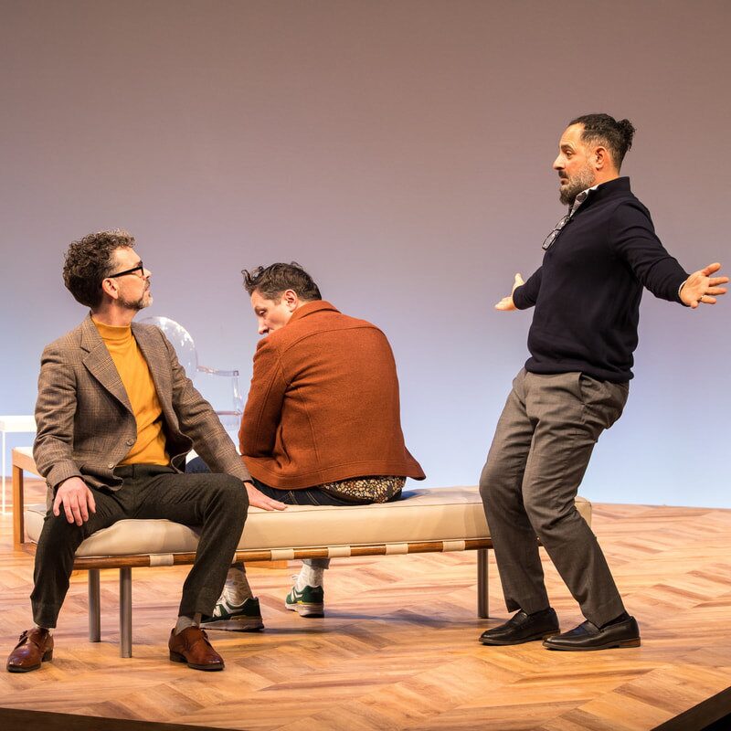 The three actors of «ART» on the white set at the Guthrie Theater: two seated on a bench, one standing with arms wide