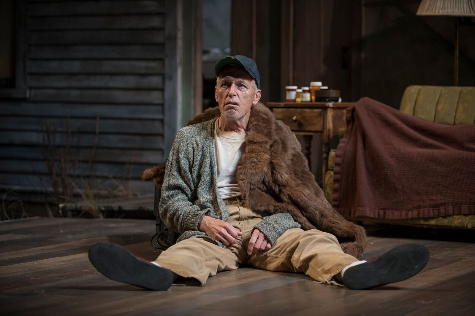 An old man sitting on the porch floor in a fur-collared coat