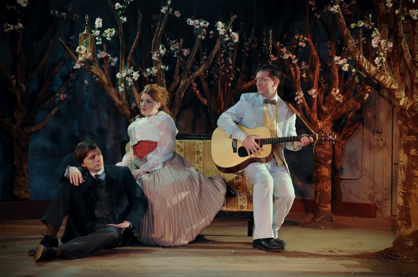 Three characters beneath blossoming trees, one playing guitar, in Cherry Orchard