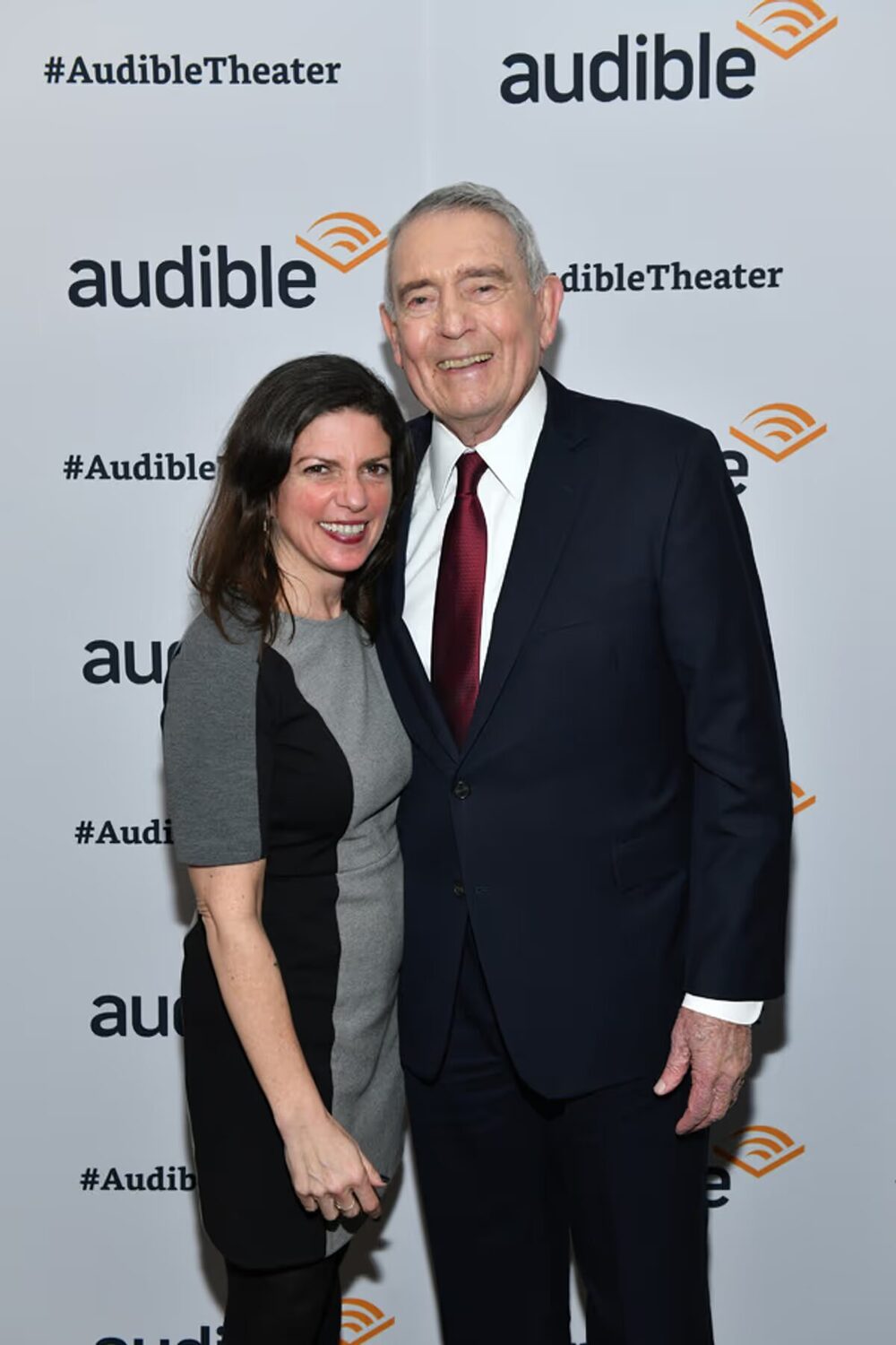 Kimberly Senior and Dan Rather smiling together in front of an Audible Theater backdrop on opening night