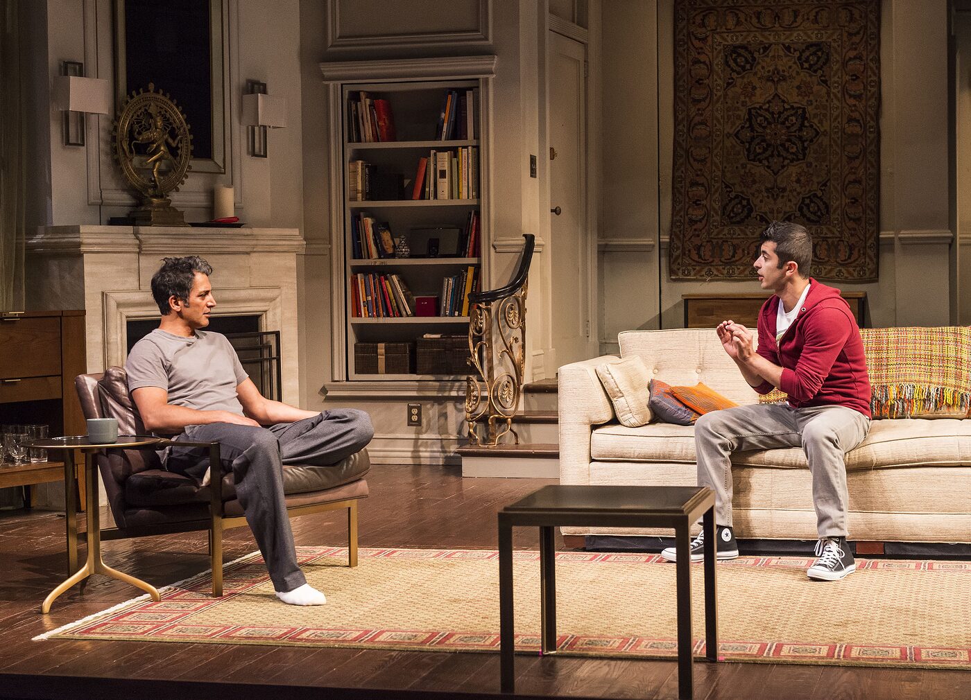 Two men in the living room of Disgraced, one in an armchair and one on the sofa