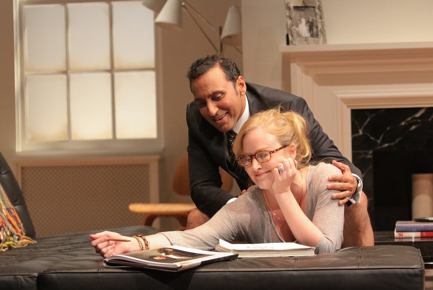 A man embraces a woman leaning over a scrapbook on the coffee table in Disgraced