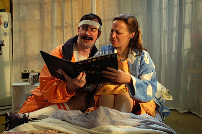 A couple reads a scrapbook together in bed in Fuddy Meers