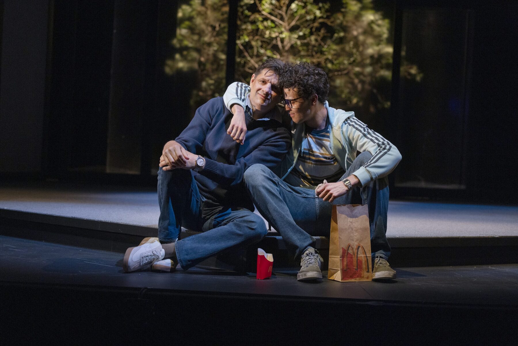 Two actors sitting on the ground, leaning on each other