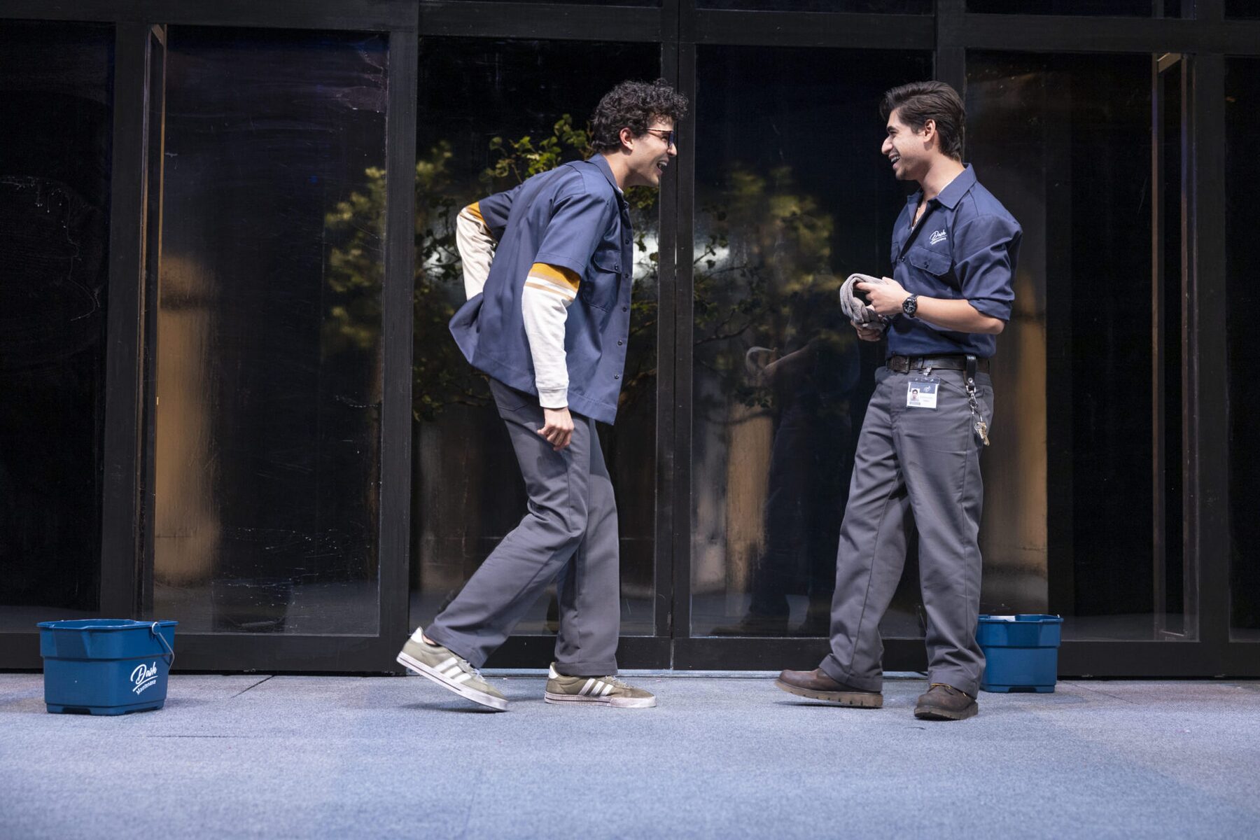 Two men in work uniforms with a mop bucket on the set