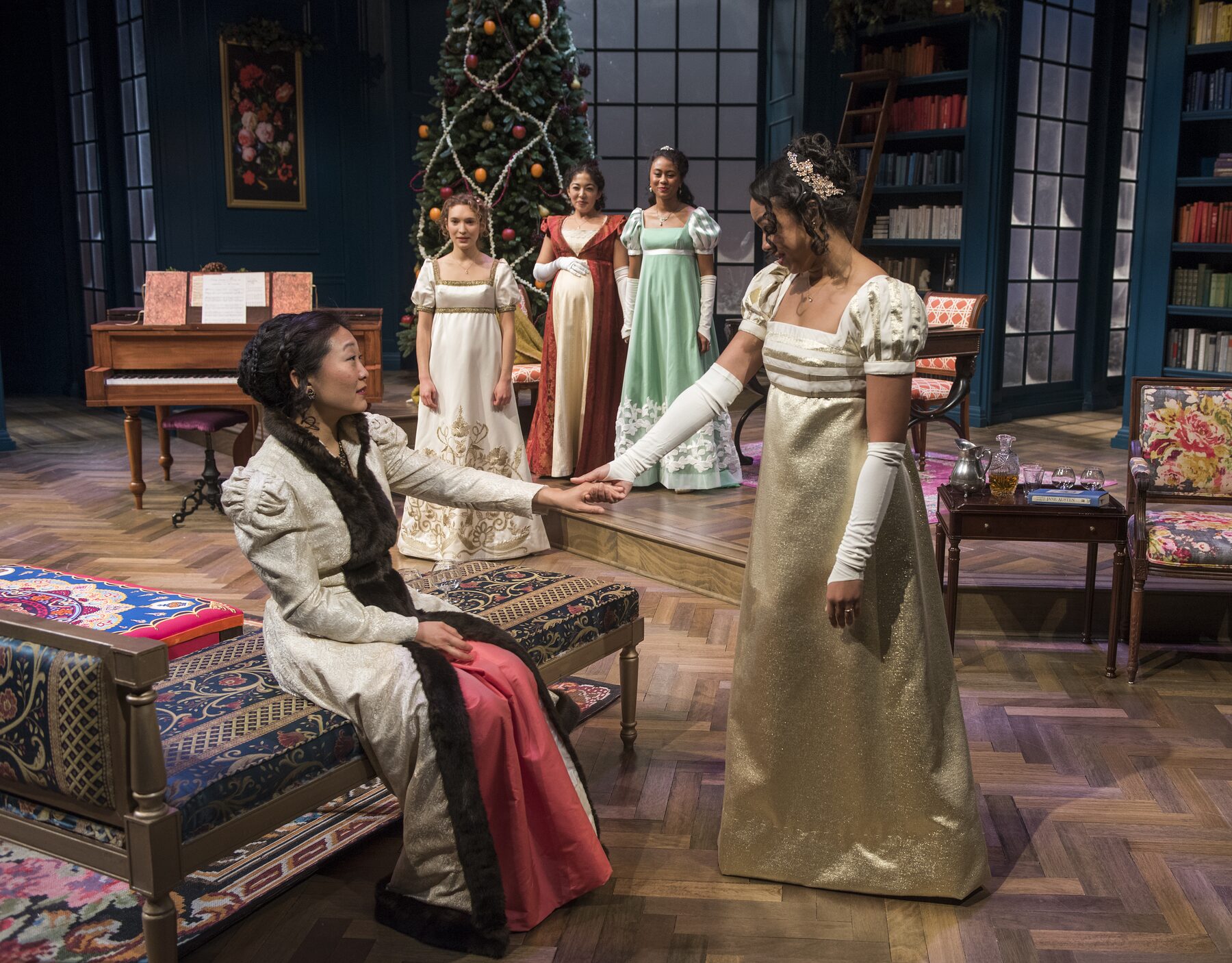 Sisters in Regency gowns beside the Christmas tree in the Pemberley library