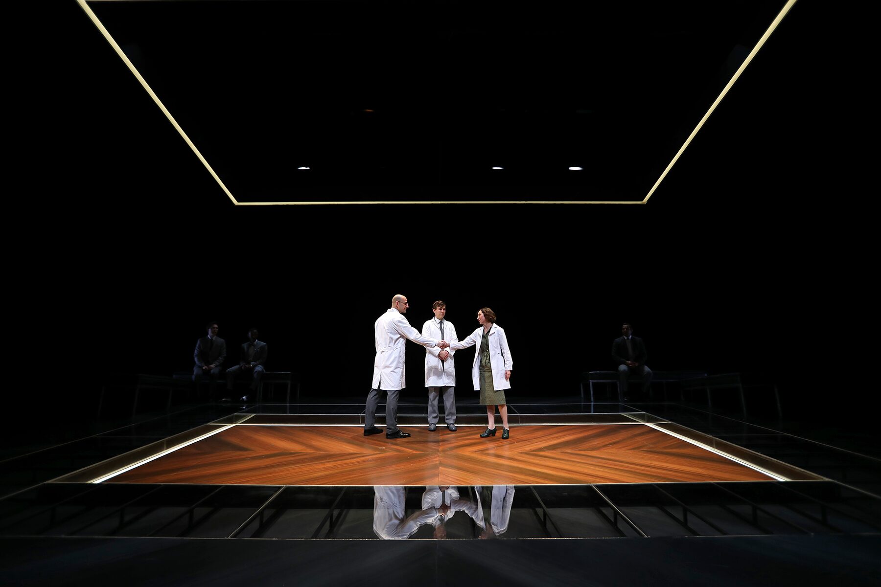 Three scientists in white coats on the wide, glowing stage