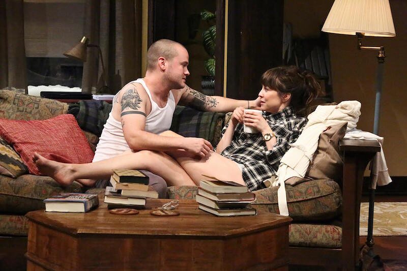 Ethan and Olivia talking on the sofa surrounded by books in Sex With Strangers