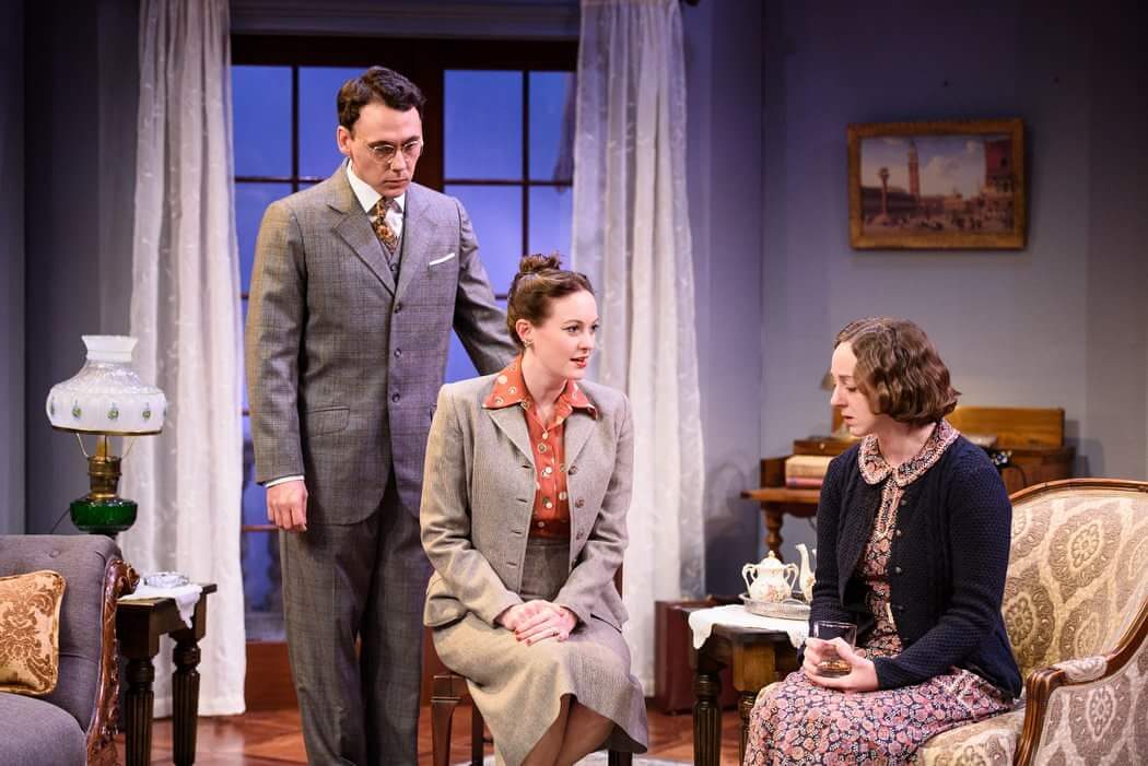 A man in a suit stands behind two seated women