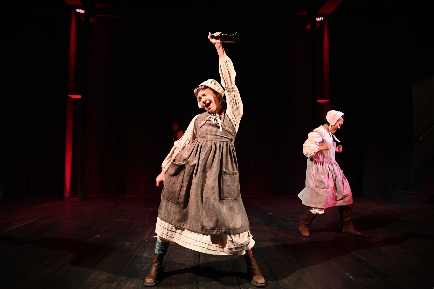 Two of the young girls in The Good John Proctor, one with an arm raised, under red light