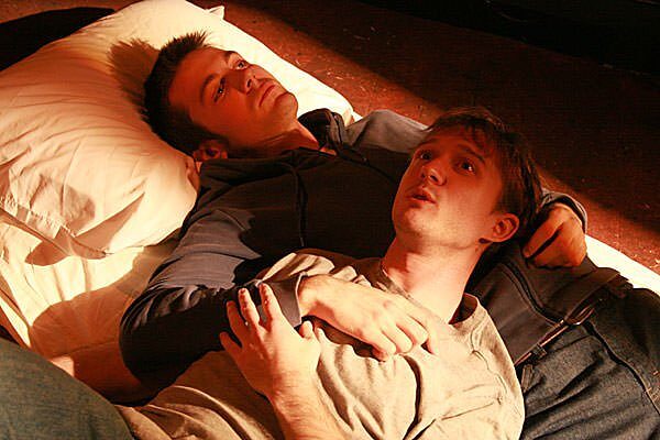 Two brothers lying together on a bed in The Pillowman