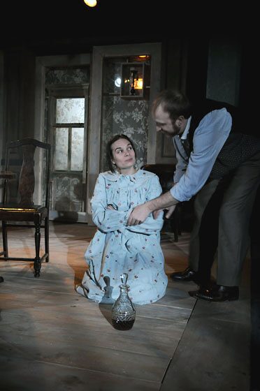 A man leans over a woman kneeling on the floor in a tense confrontation in Uncle Vanya