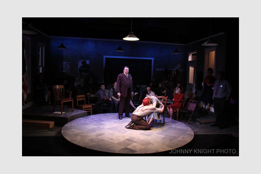 A wide view of the union hall set, with a couple embracing at center, in Waiting for Lefty